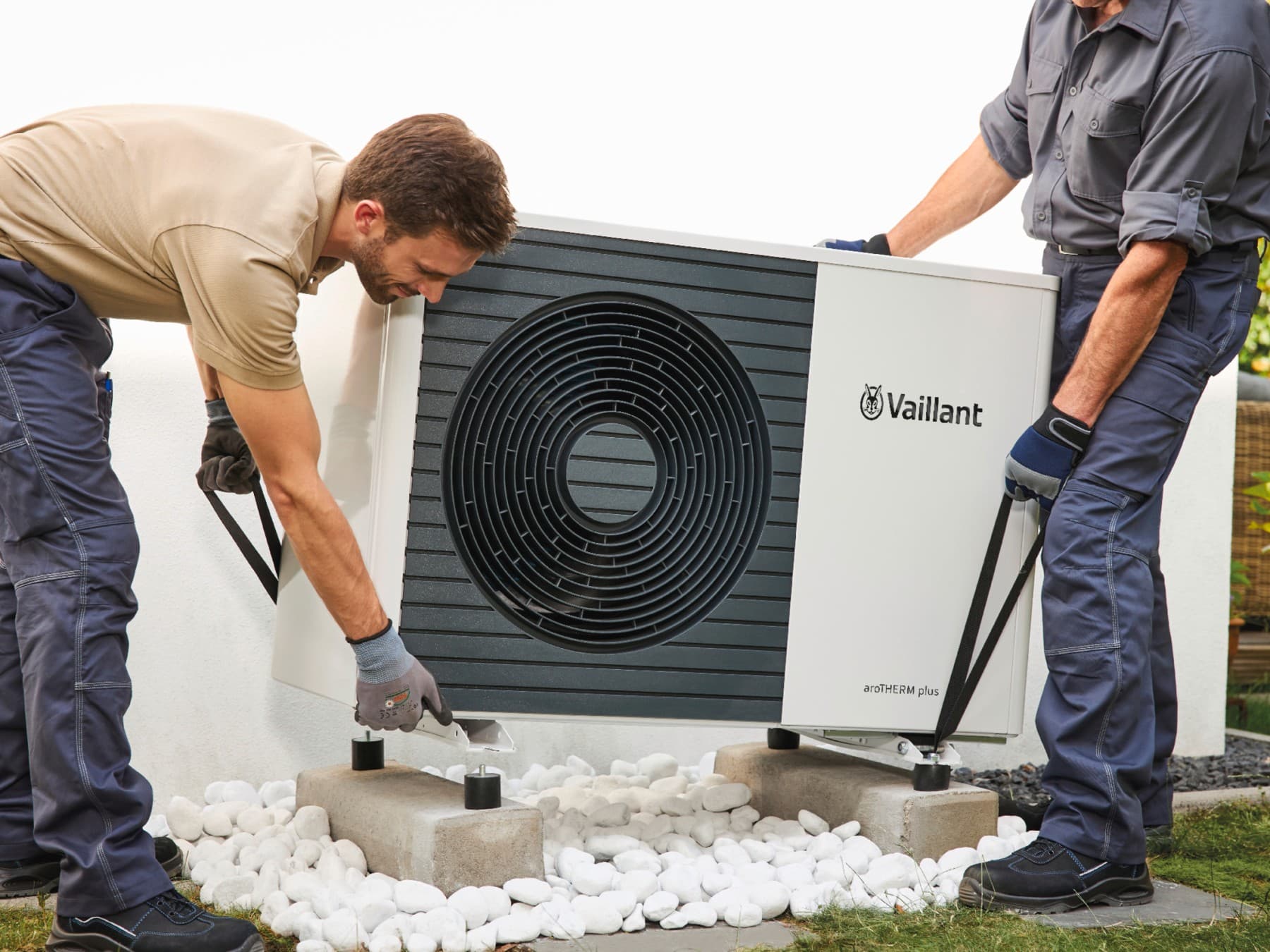 Deux installateurs posent une unité extérieure de pompe à chaleur sur une terrasse | Vaillant