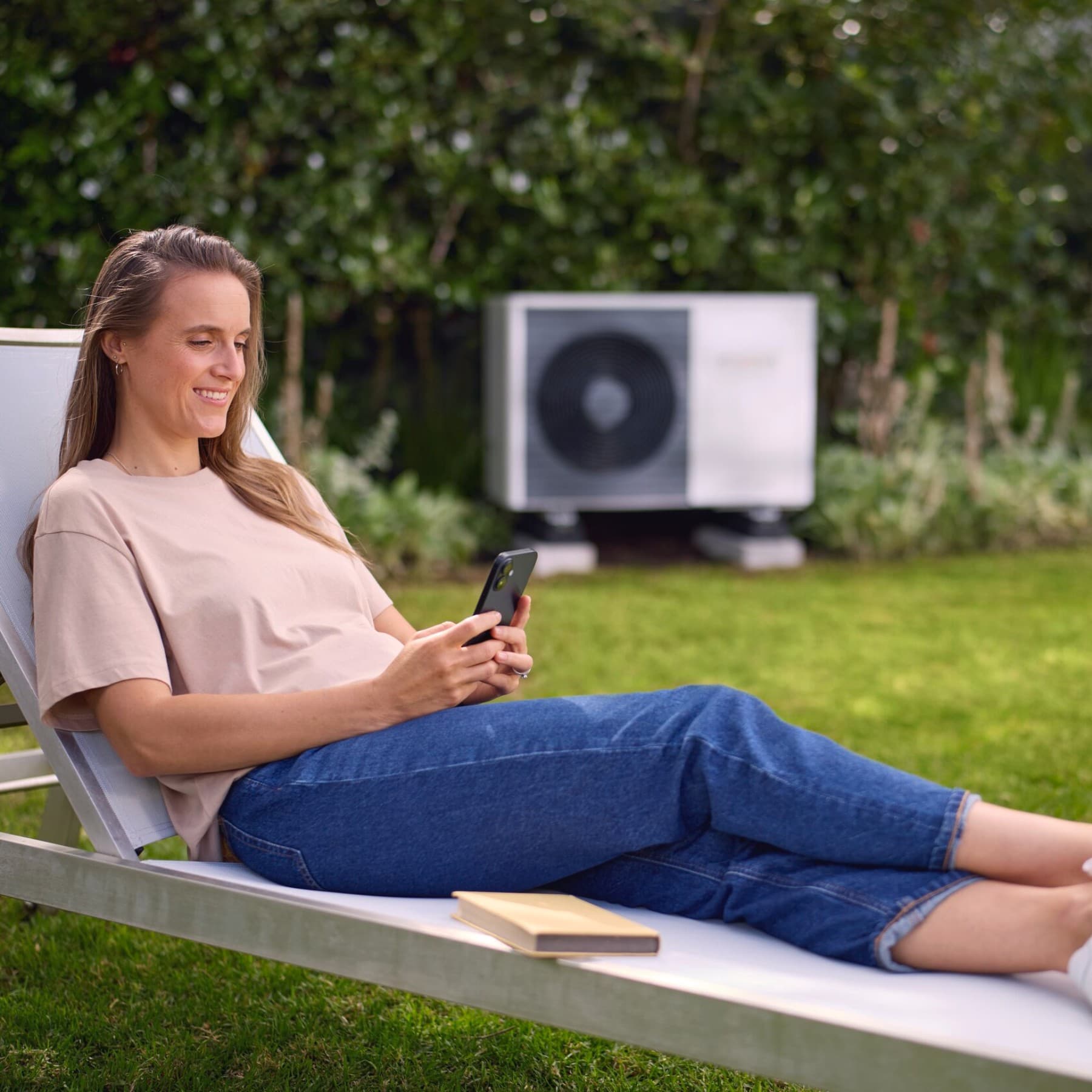Femme allongée sur un transat dans un jardin devant une pompe à chaleur | Vaillant